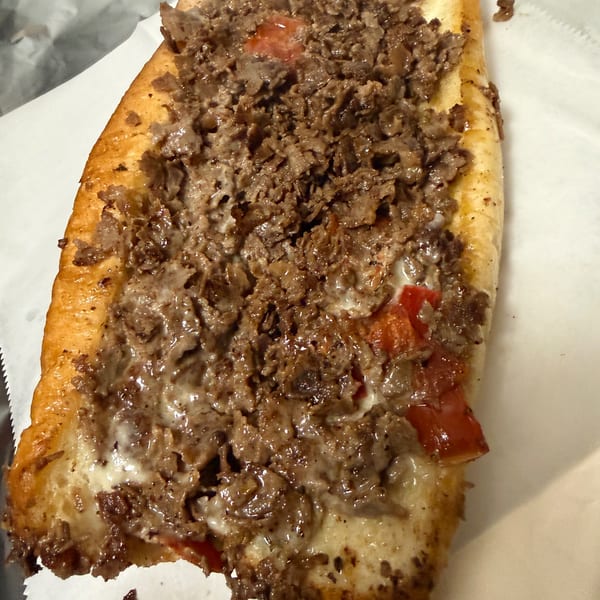 A close-up of a delicious cheesesteak sandwich with melted cheese, steak, and red peppers.