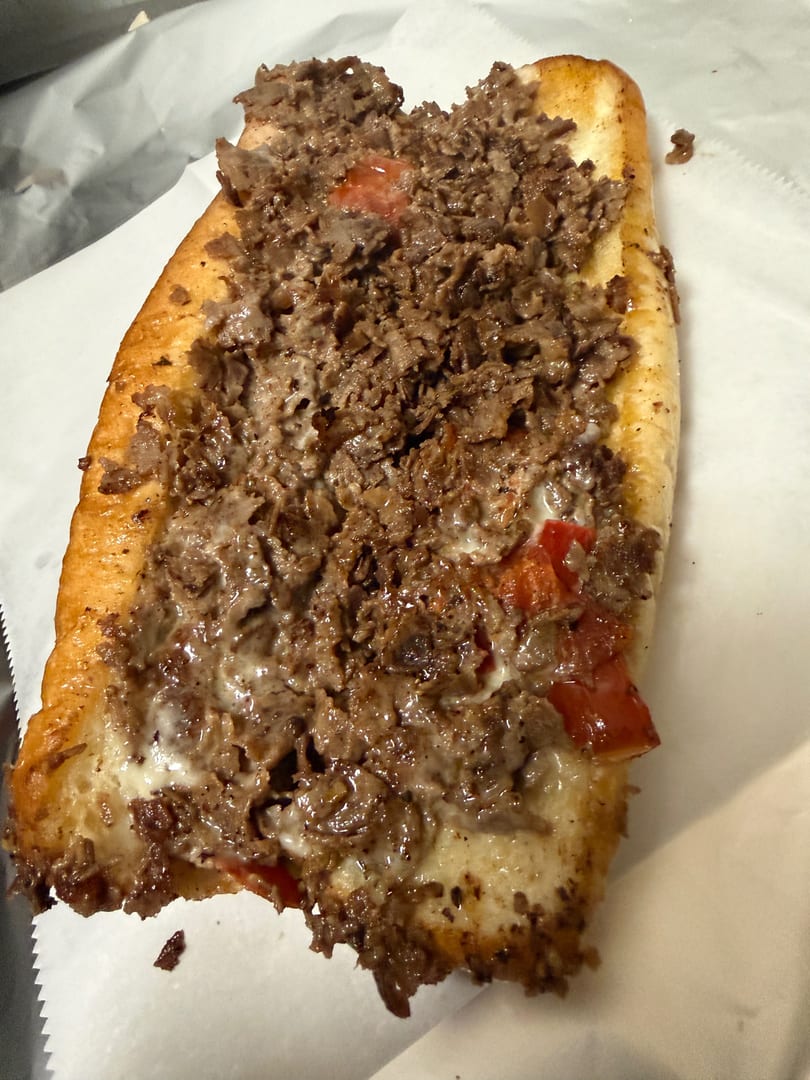A close-up of a delicious cheesesteak sandwich with melted cheese, steak, and red peppers.