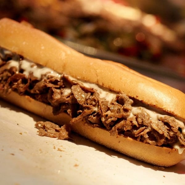 Close-up of a delicious cheesesteak sandwich with melted cheese and thinly sliced meat on a bun.