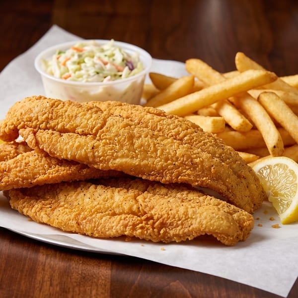 Golden-fried fish fillets, french fries, coleslaw, and lemon wedges on white paper.