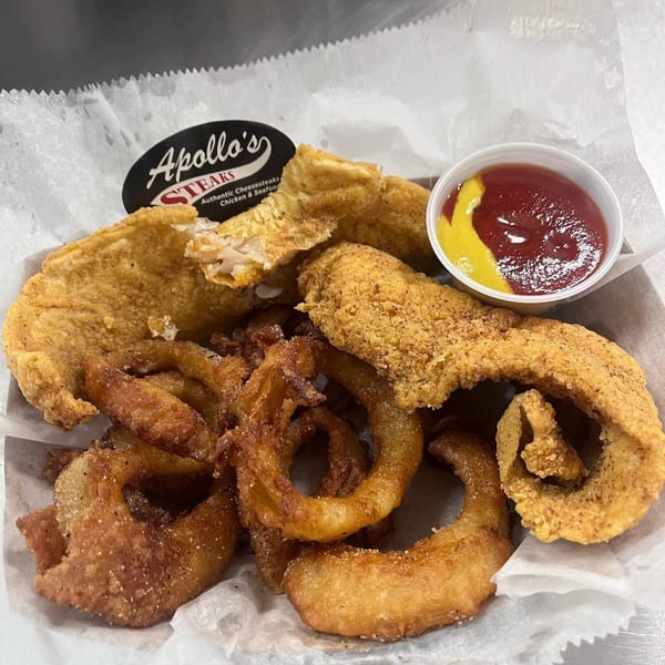 Apollo's Steaks fried fish and onion rings with ketchup and mustard in a white paper-lined basket.