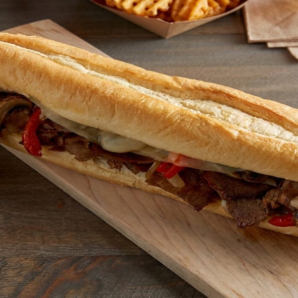 Cheesesteak sandwich with steak, mushrooms, peppers, and melted cheese on a wooden board.