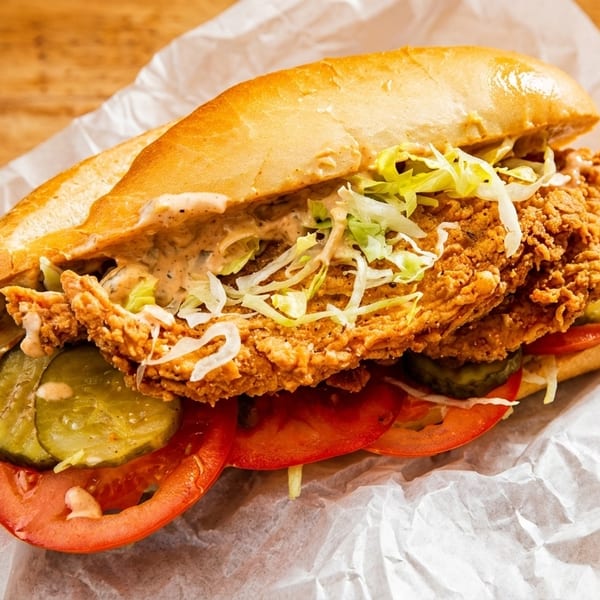 Crispy fried chicken sandwich with lettuce, tomatoes, pickles, and sauce on a bun.