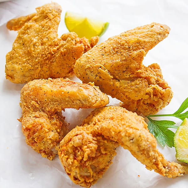 Crispy fried chicken wings seasoned with pepper, garnished with lime wedges and parsley.